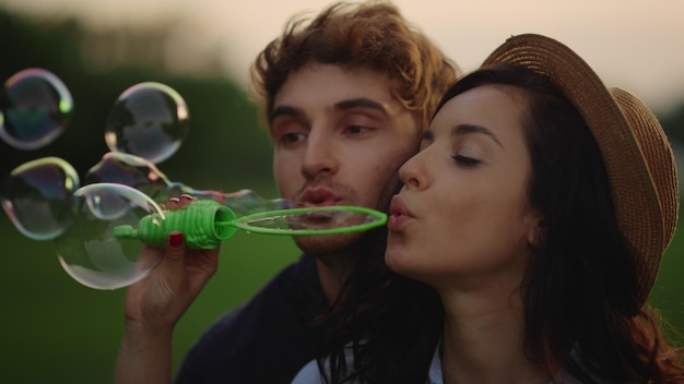 Cute girl and guy throwing bubbles on field Couple blowing soap bubbles