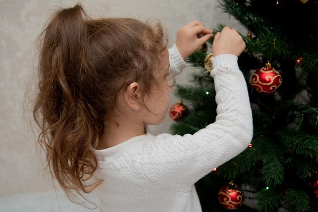 A cute girl hangs a toy on the Christmas tree