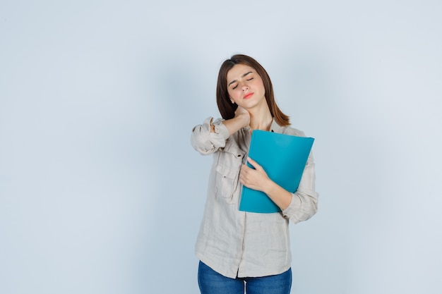 Cute girl holding folder, feeling neck pain in shirt and looking fatigued.