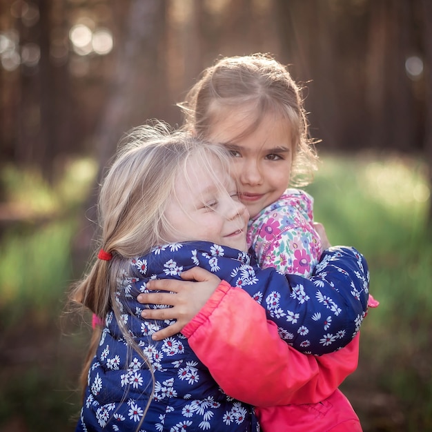 Photo cute girl hugging her small sister with love and tenderness during their walking in the forest at autumn, national hug and friendship day, casual lifestyle, outdoor