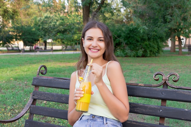 Cute girl is relaxing in the park and drinking cool juice in a hot day