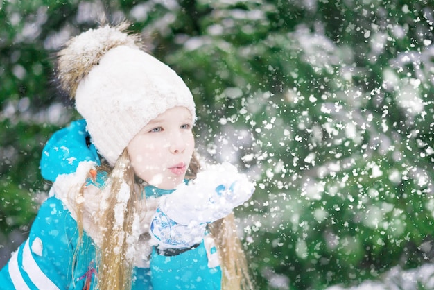 A cute girl kid blowing the snow from her hand