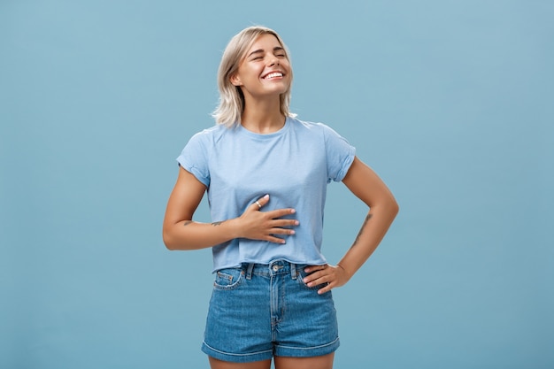 Cute girl likes eat after workout being pleased and stuffed after dinner. Portrait of satisfied attractive blonde young woman touching belly raising head up with broad smile