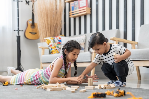 Cute girl and little boy play wood blocks stacks game on floor in living room at home