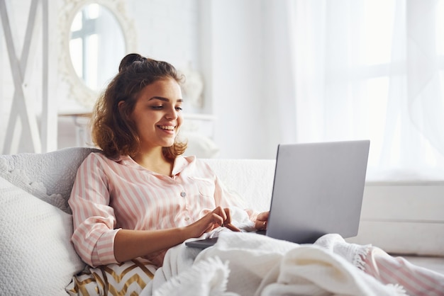 Cute girl lying on the bed with laptop in the bedroom at her weekend time.