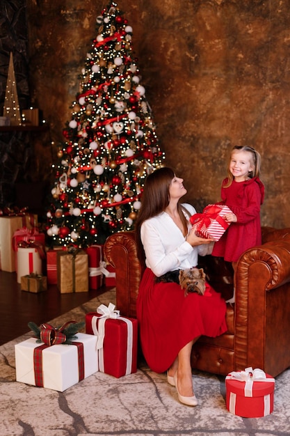 Cute girl and mom at home near the christmas tree with gifts