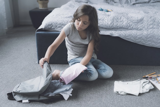 Cute Girl Packing Bag Sits on Floor in Bedroom