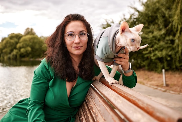 Cute girl petting a furry cat outdoor Sitting on wooden bench with green trees and river background Love to the animals