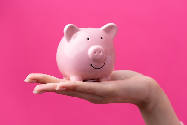 A cute girl in a pink jacket is holding a 3d piggy bank in her hands Beautiful closeup portrait in studio on pink