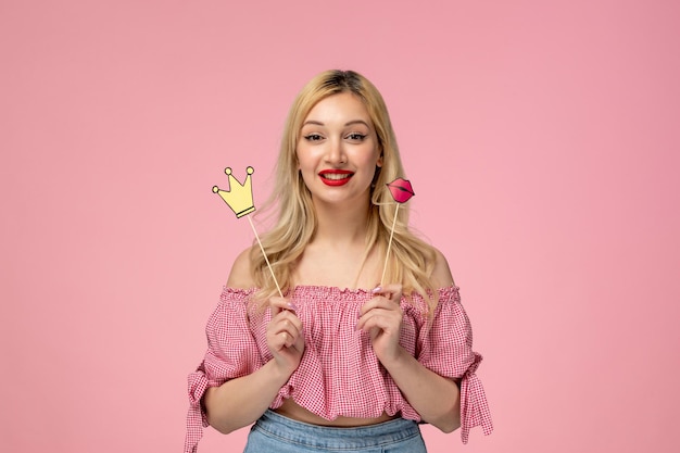 Cute girl pretty blonde lady wearing red lipstick in pink blouse holding requisites lips crown