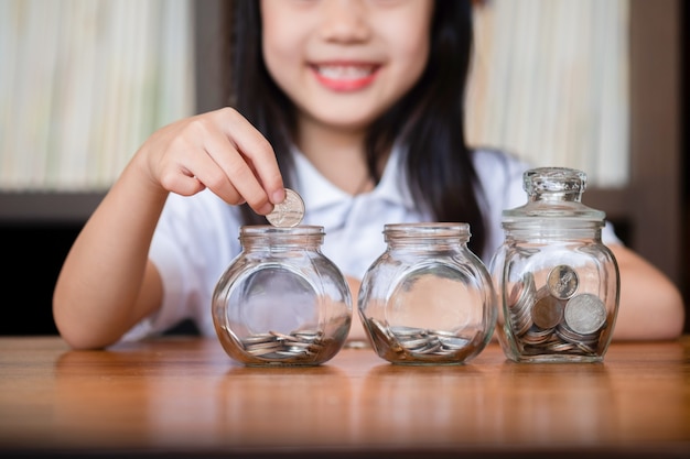 Cute girl putting money coins in glass,saving money concept