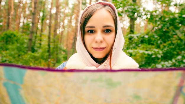 Cute girl reading map in forest Traveling woman with backpack with open map in woods