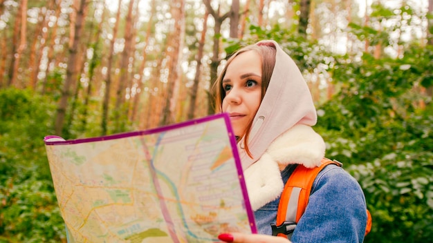 Cute girl reading map in forest Traveling woman with backpack with open map in woods