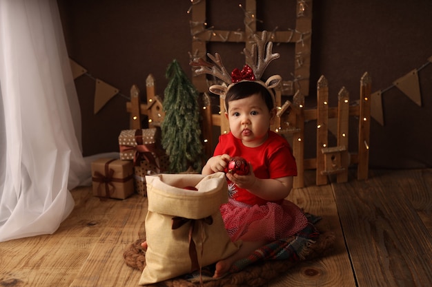 a cute girl in a red Christmas costume takes out Christmas tree toys from a bag with gifts