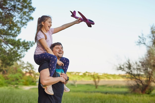 Cute girl riding on father's shoulder playing with toy airplane