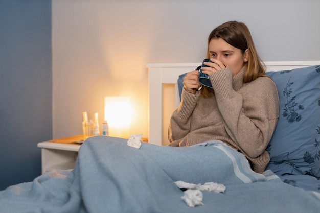 Cute girl sitting in bed under blanket and drink remedy for heat temperature Woman feeling sick