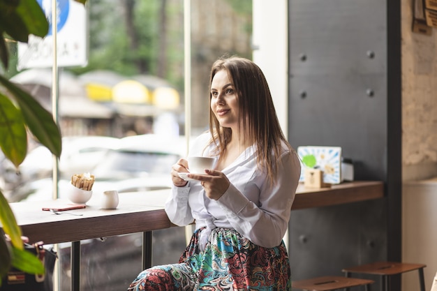 cute girl sitting in cafe with cup of coffee in hands