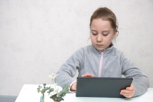 Cute girl sitting at the table works in the tablet online learning