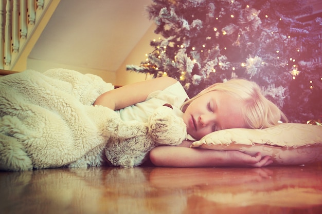 Cute girl sleeping on floor under Christmas tree