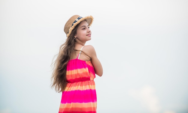 Cute girl in summer dress and hat outdoors sky background Happy vacation Happy childhood Enjoying relax Child happy small girl Free and carefree Good vibes Happy international childrens day