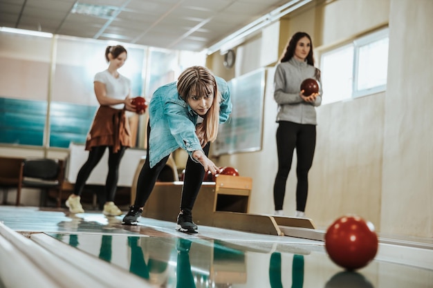 A cute girl throwing the bowling ball while her friends are standing in the back.