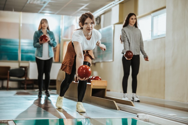 A cute girl throwing the bowling ball while her friends are standing in the back.