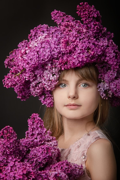 Cute girl with blonde hair in a pink dress with a bouquet of lilacs on a black background