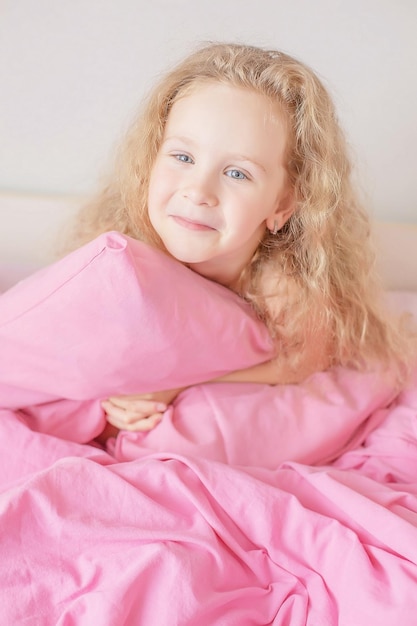 cute girl with blue eyes and curly hair hugs a pink pillow house