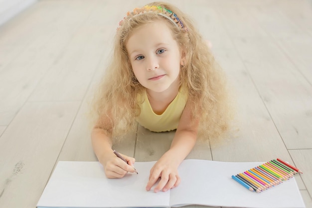 a cute girl with curly hair and blue eyes draws in an album with colored pencils