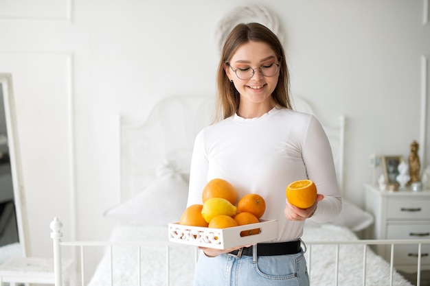 Cute girl with glasses holds a fruit basket and smiles in a white room