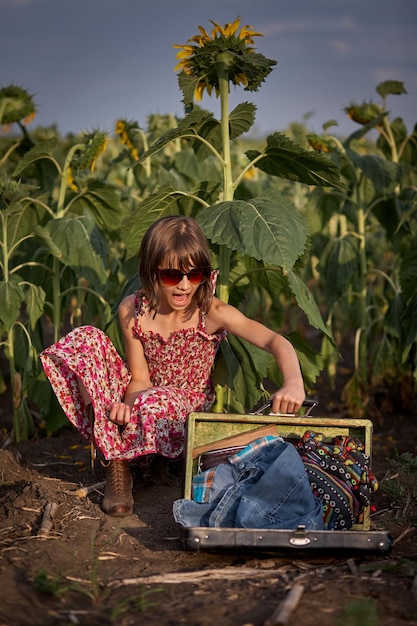 Cute girl with old suitcase in a sunflower field