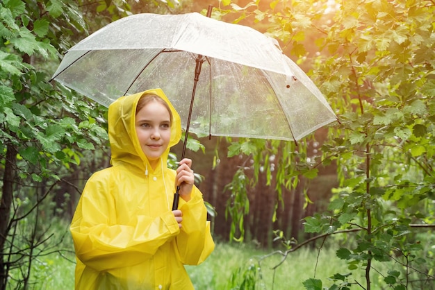 Cute girl in yellow raincoat holds umbrella on rainy day