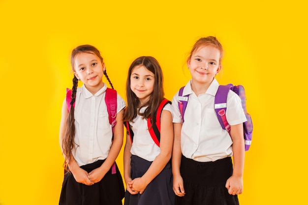 Cute girls in uniform with backpacks on yellow background