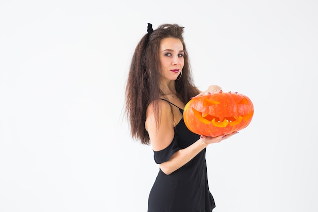 Cute gothic woman in halloween style clothes with pumpkin in hands over light wall with copy space