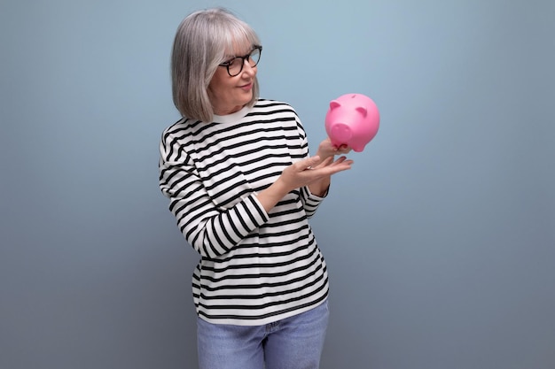 Cute grandmother old woman s holding a piggy bank with a pension on a bright background with copy