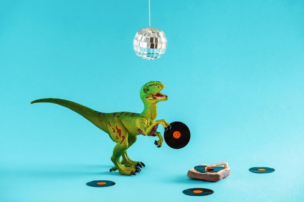 Cute green dinosaur toy holding a vinyl record and listen vinyl on vinyl record player on a blue