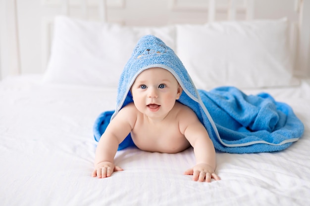 A cute happy laughing baby after a bath is playing on a white bed in a spacious children's room The child is in a clean and dry towel Washing baby hygiene health and skin care