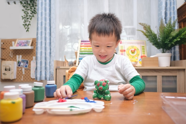 Cute happy little Asian 3 - 4 years old toddler boy child  painting color on DIY plaster painting toy, 3D plaster statue indoor at home, Creative play for kids and toddlers concept - Selective focus