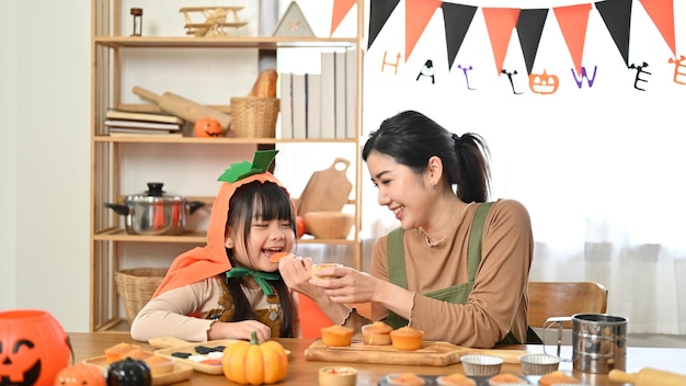 Cute and happy little Asian girl eating a yummy Halloween cupcake with her mom