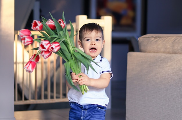 Cute happy little boy holding bouquet of red tulips. Mothers or Valentine Day. 