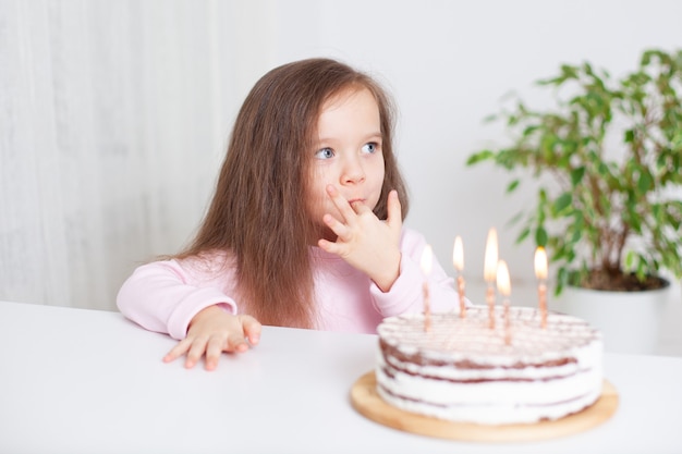 A cute happy little girl with blond hair and blue eyes licks the cream with a finger birthday