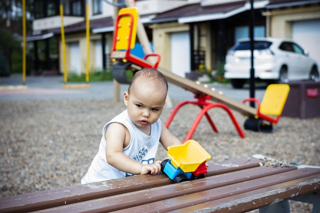 Cute happy smiling baby boy playing with colorful toy car at children playground outdoors