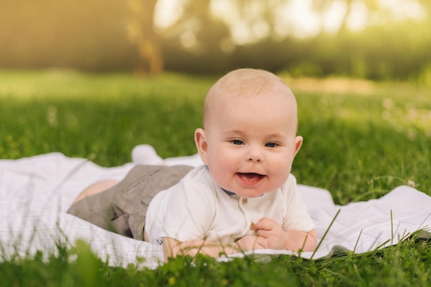 Cute happy toddler lying on a blanket on the grass outdoors in summer