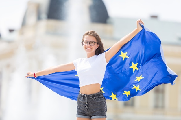 Cute happy young girl with the flag of the European Union in front of a historic building somewhere in europe.