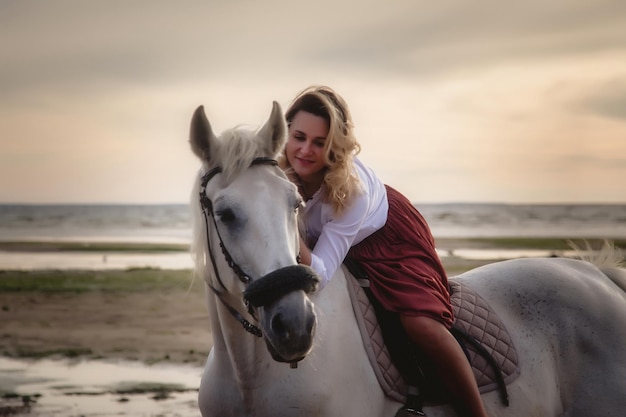 Cute happy young woman on horseback in summer beach by sea