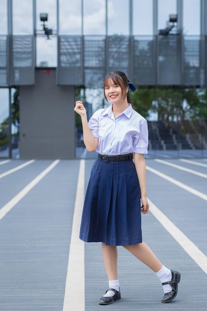 Cute high school Asian student girl in school uniform stands and smiles happily while confidently