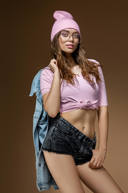 Cute hipster girl in jeans shorts a pink hat and stylish glasses