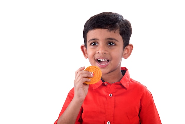 Cute Indian kid eating murukku or chakli on a white background