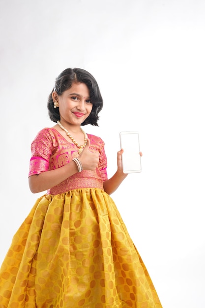 Cute indian little girl showing smartphone screen on white background