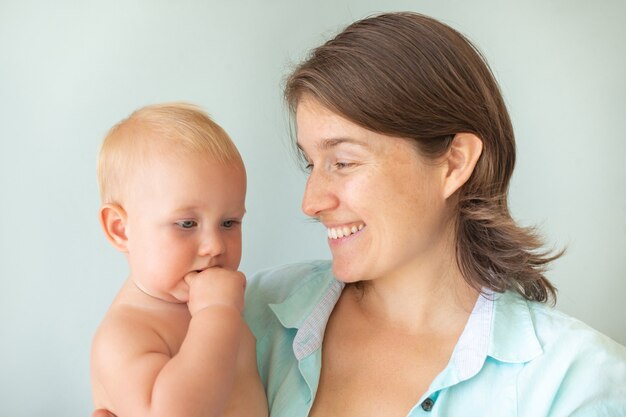 Cute infant baby on mothers hands on a gray background. Mother hugging baby with love. Motherhood concept. Unconditional love.